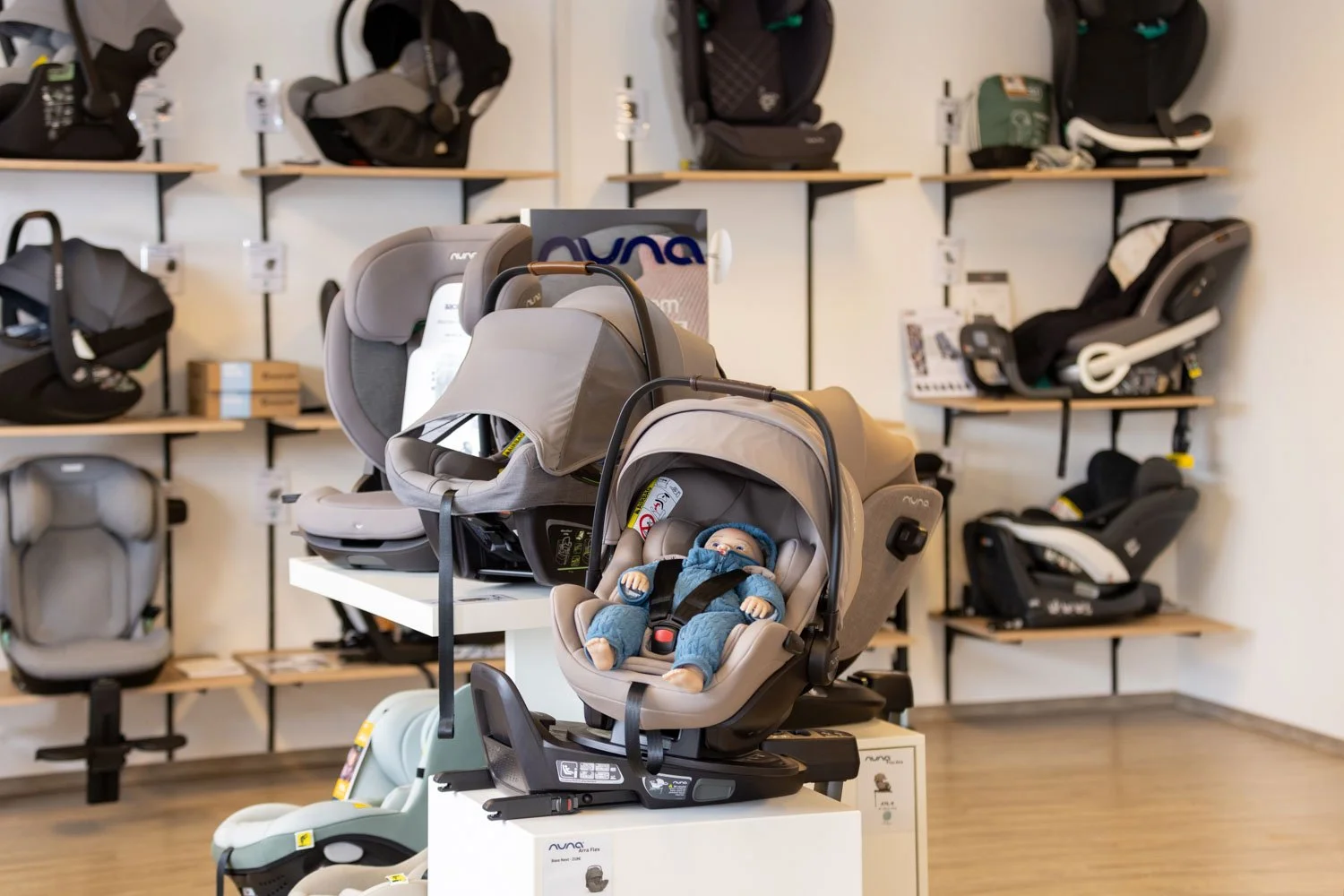 Autositz für Babys in einem Fachgeschäft, umgeben von weiteren Autositzen an den Wänden.