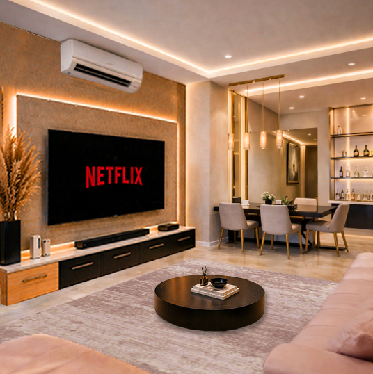 Modern living room with a wall-mounted TV displaying the Netflix logo, a beige accent wall, a low black TV stand, a round black coffee table, a pink sofa, a dining table with six chairs, and a built-in bar with bottles and glasses, illuminated by warm lighting.