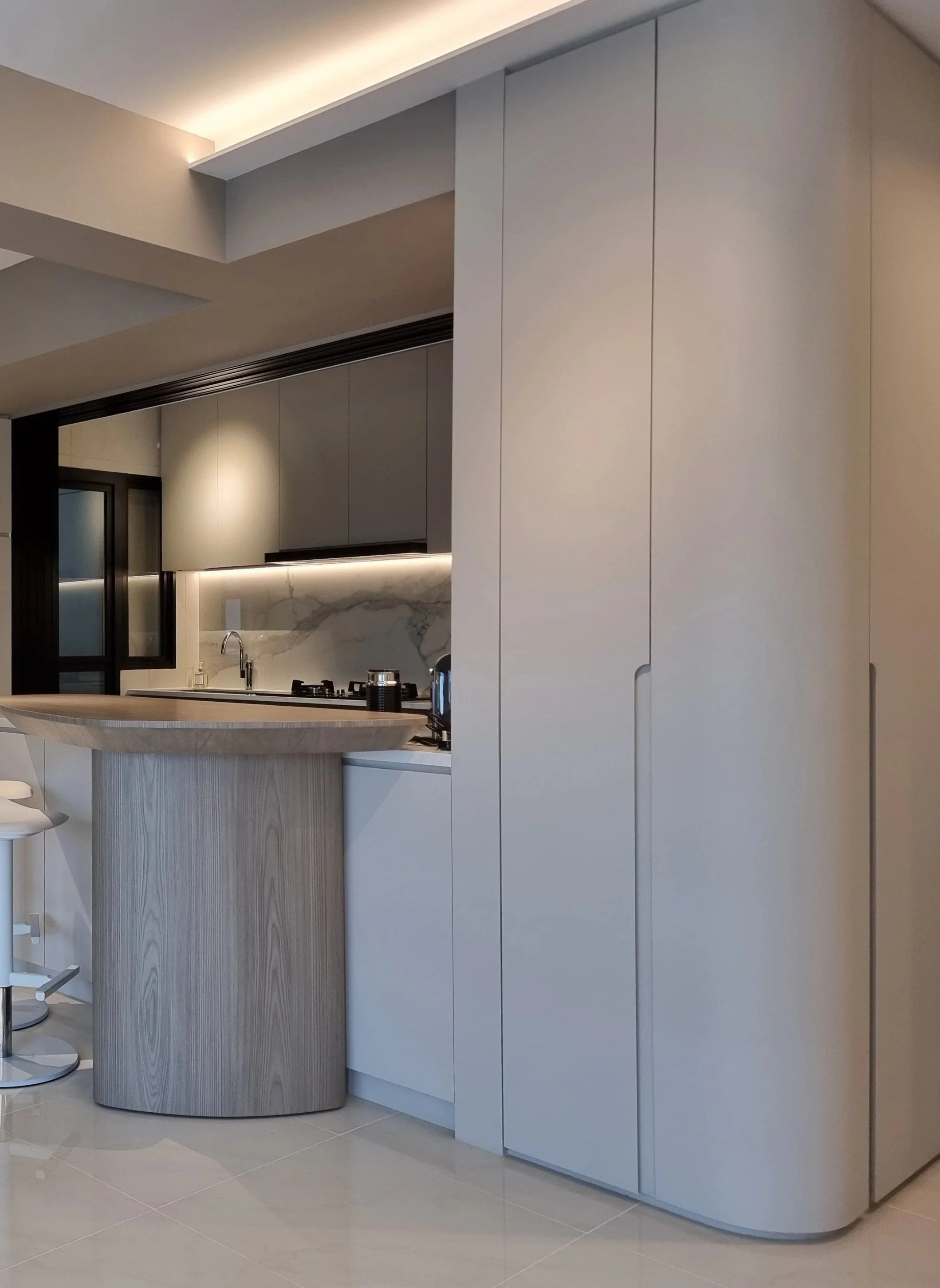 Modern kitchen with beige cabinets, marble backsplash, and a curved wooden kitchen island with barstools.