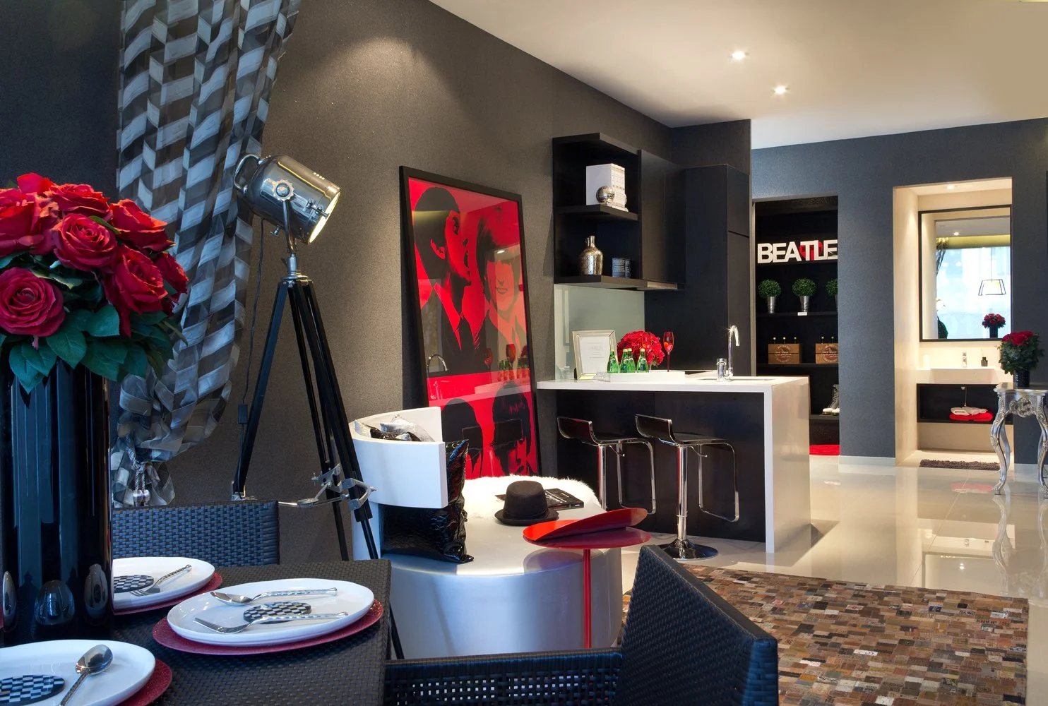 Modern dining and kitchen area with black and white decor, red flowers, artwork on the wall, and a black tripod lamp.