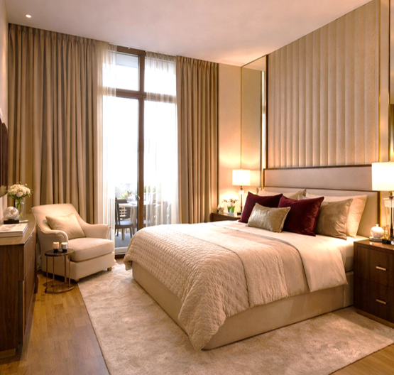 Elegant hotel bedroom with a large bed, nightstands with lamps, an armchair, and a balcony with glass doors and curtains