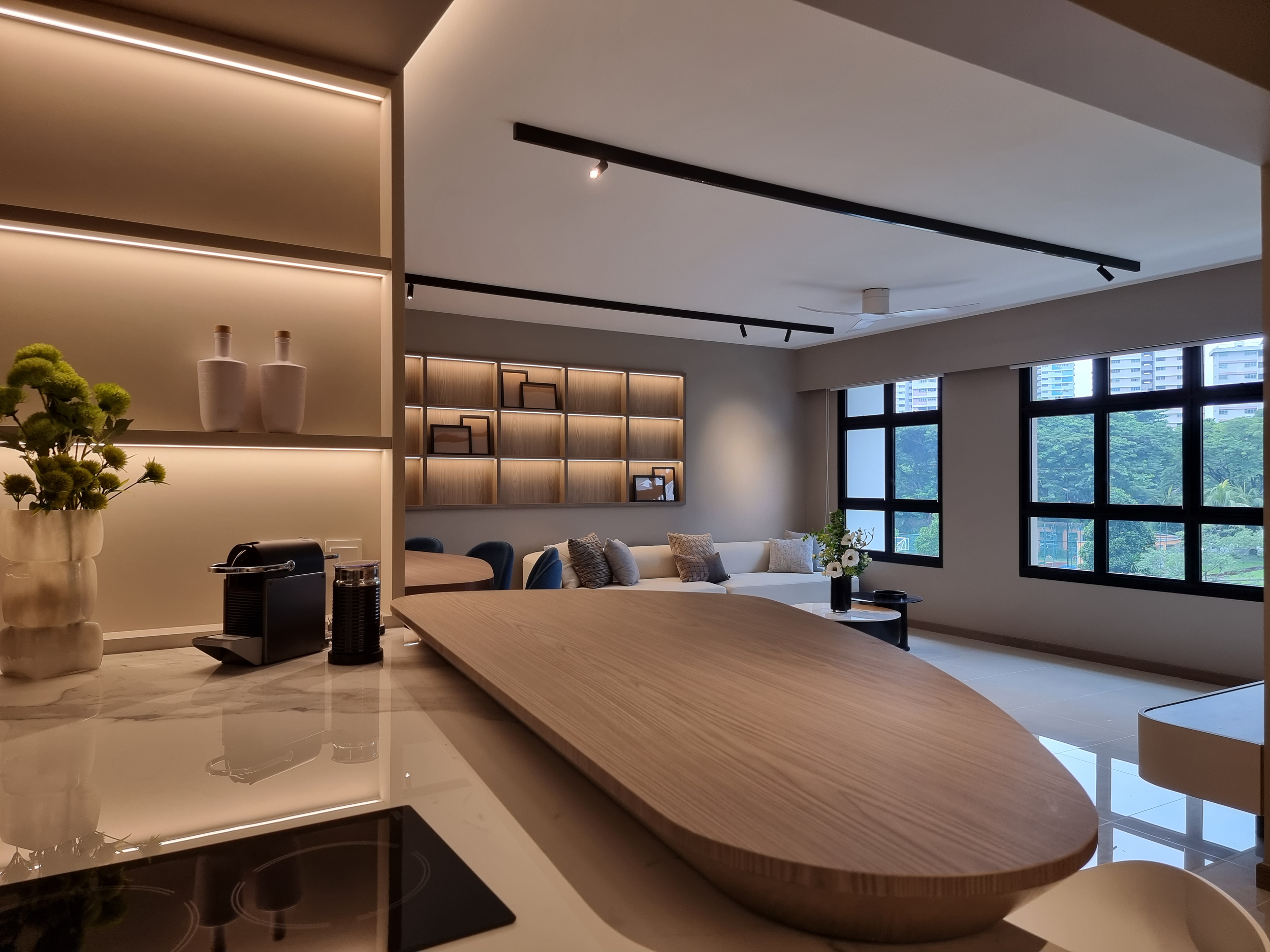 Modern living room with a large white sofa, wooden coffee table, and large windows showing city buildings outside.