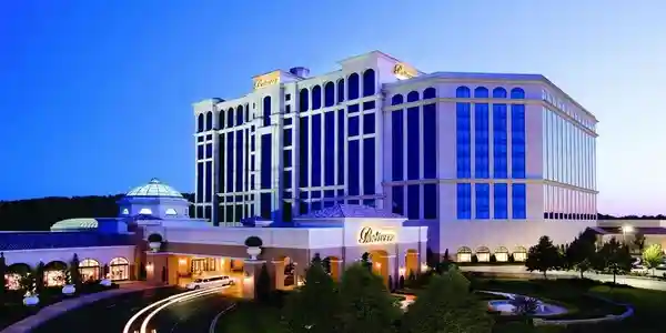 A large, modern hotel building with a sign that says 'Plaza,' illuminated at night, with surrounding trees and a curved driveway.
