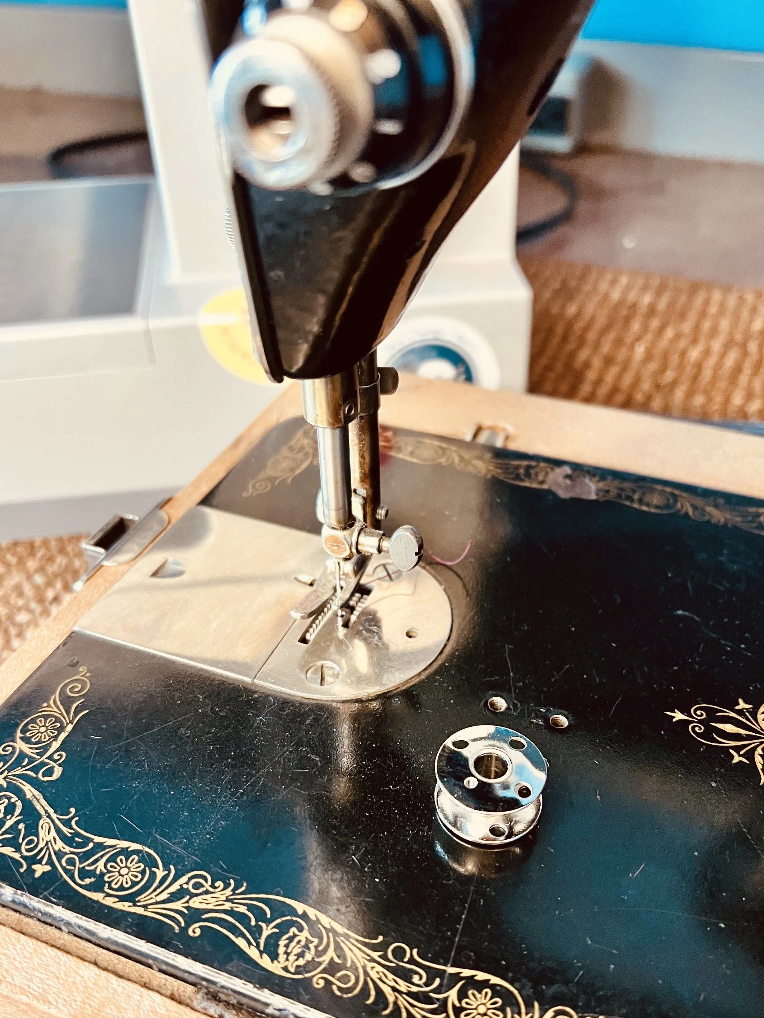 Close up on the shank of an antique Singer sewing machine with a metal Class 66 bobbin placed next to the needle plate