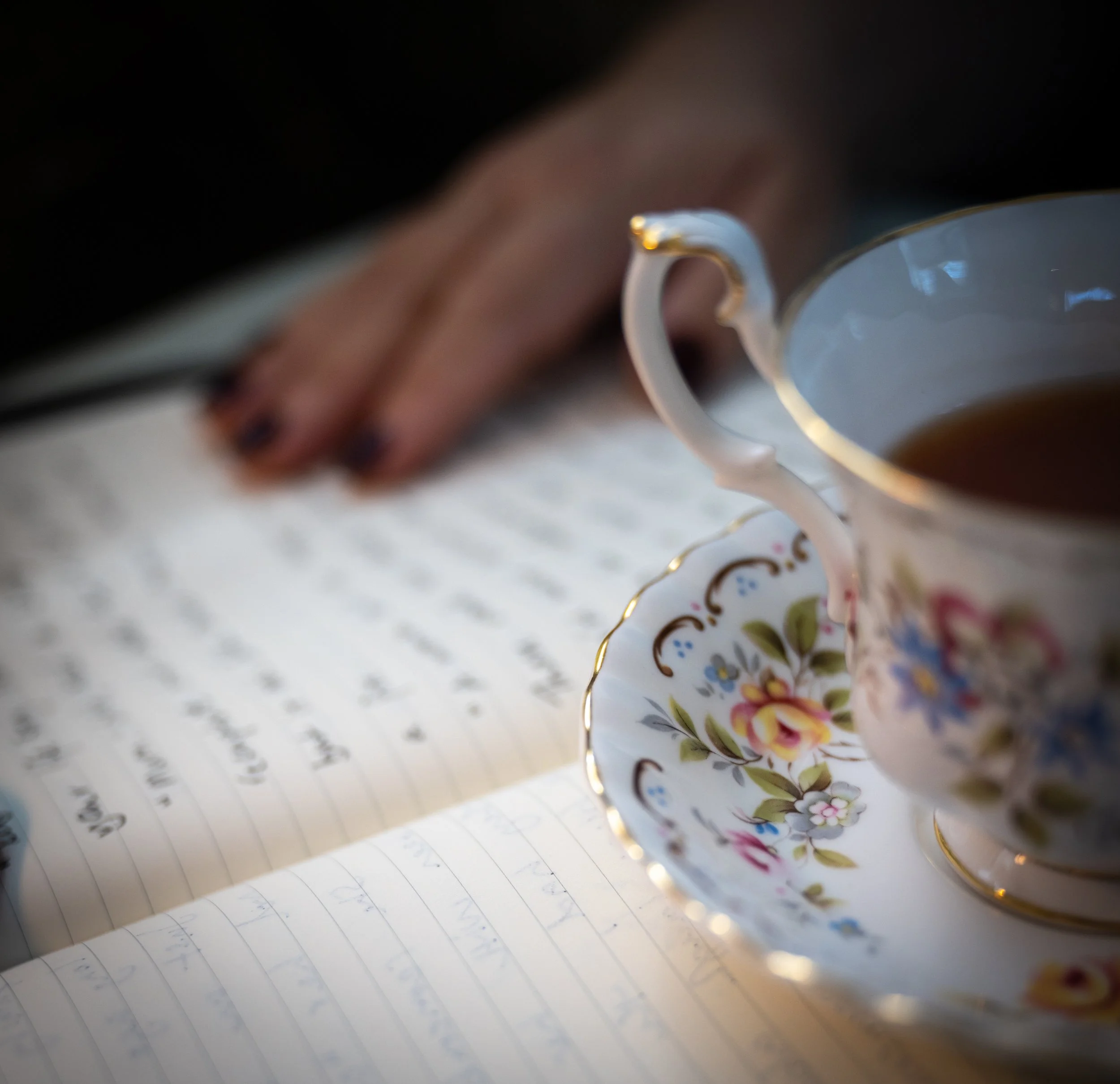 Tea cup sitting on a notebook with a woman's hand in the background.