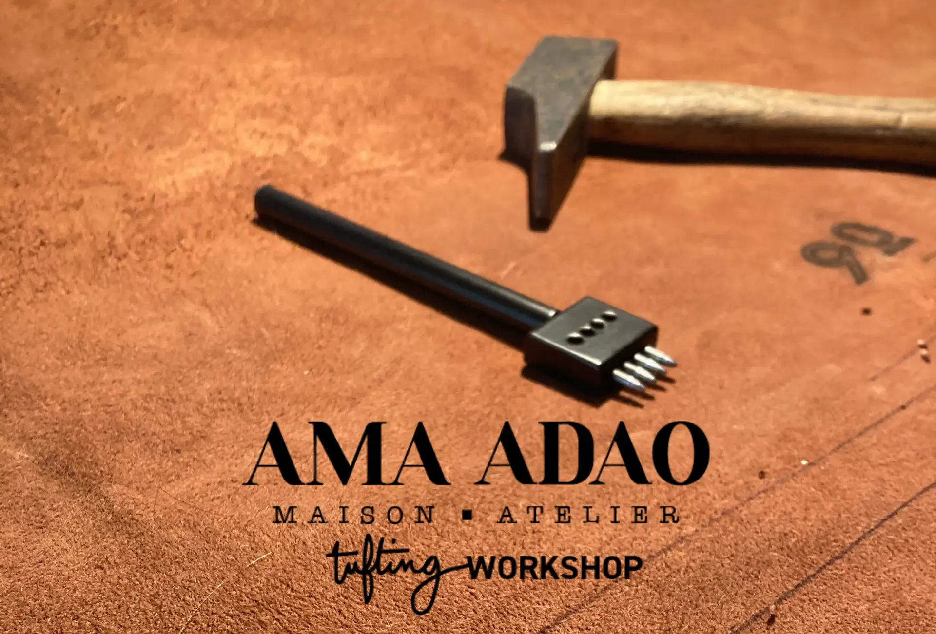 Une table en cuir marron avec un marteau en bois et un outil à 6 broches en métal noir posés dessus. Du texte en français et en anglais: "AMA ADO MAISON ATELIER tufting WORKSHOP".