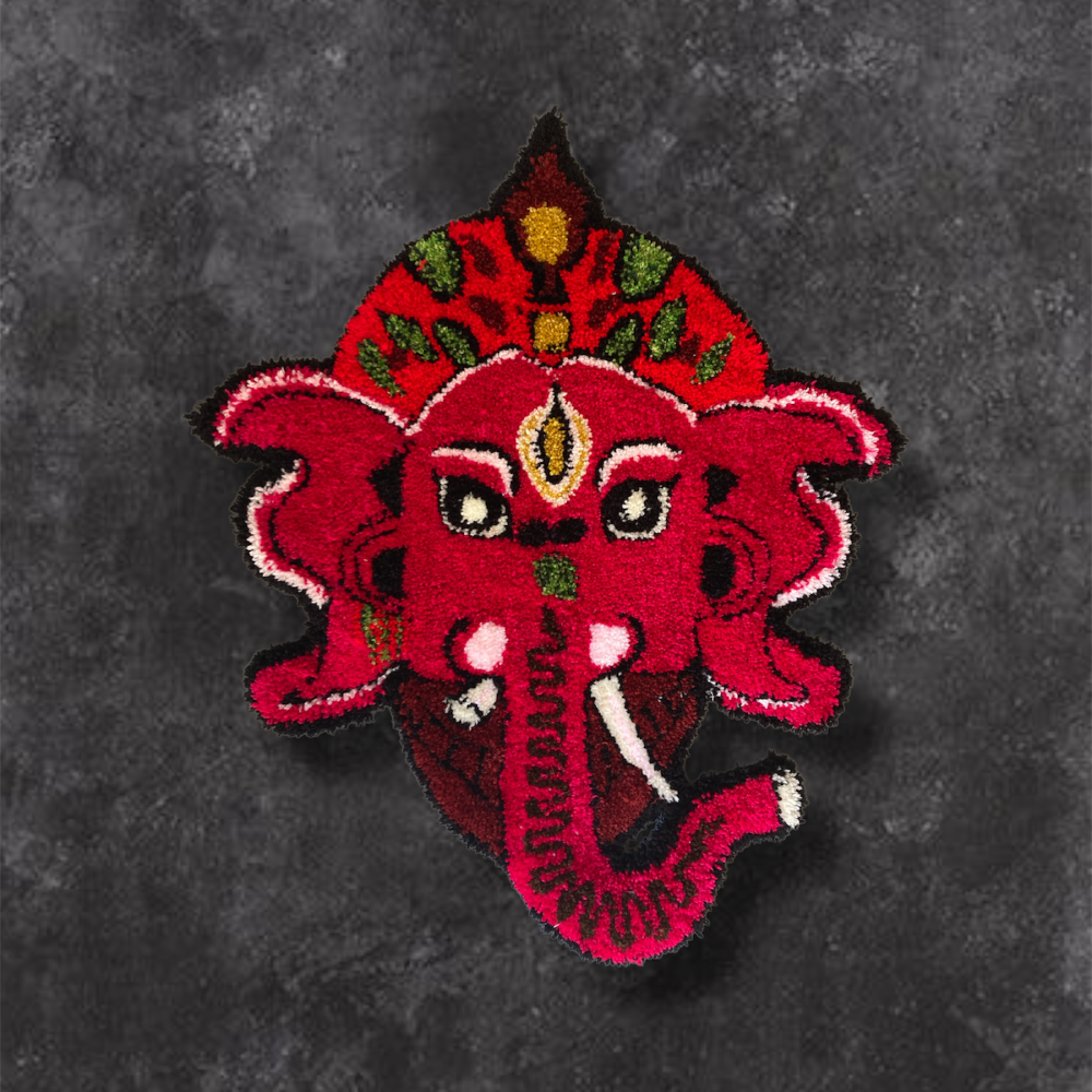 Un tapis mural en forme de Ganesh, la tête d'un éléphant symbole indien, faite de laine rose, avec des détails en vert, noir, blanc et jaune. Cette pièce a été réalisé sur mesure par Chloé Fortunet de la Maison et Atelier AMA ADAO.