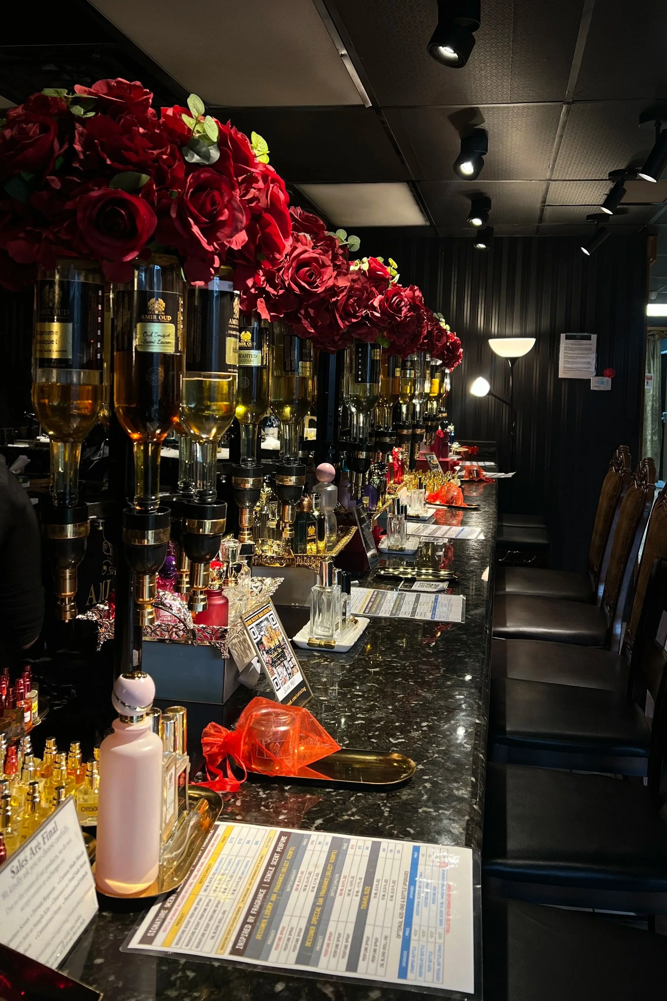 Decorated bar counter with red floral arrangements, champagne glasses, bottles, and bar menus in a dimly lit setting.