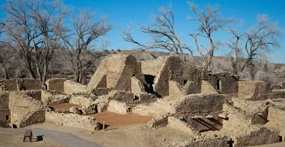 Ruins of an old adobe building with leafless trees and a bright blue sky in the background.