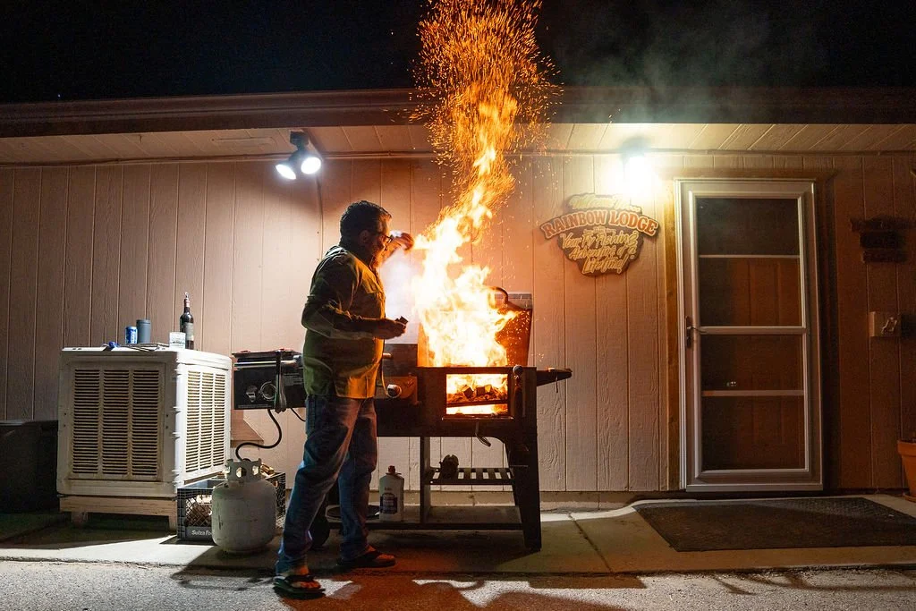 A man grilling on a barbecue grill that caught on fire at night outside a house.