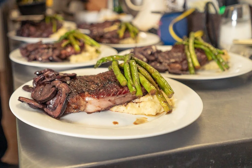 Plates of cooked steak with green beans and mashed potatoes at a dinner table.