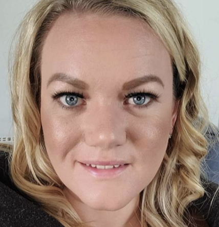 Close-up of a woman with blonde hair, blue eyes, and light makeup, smiling slightly.