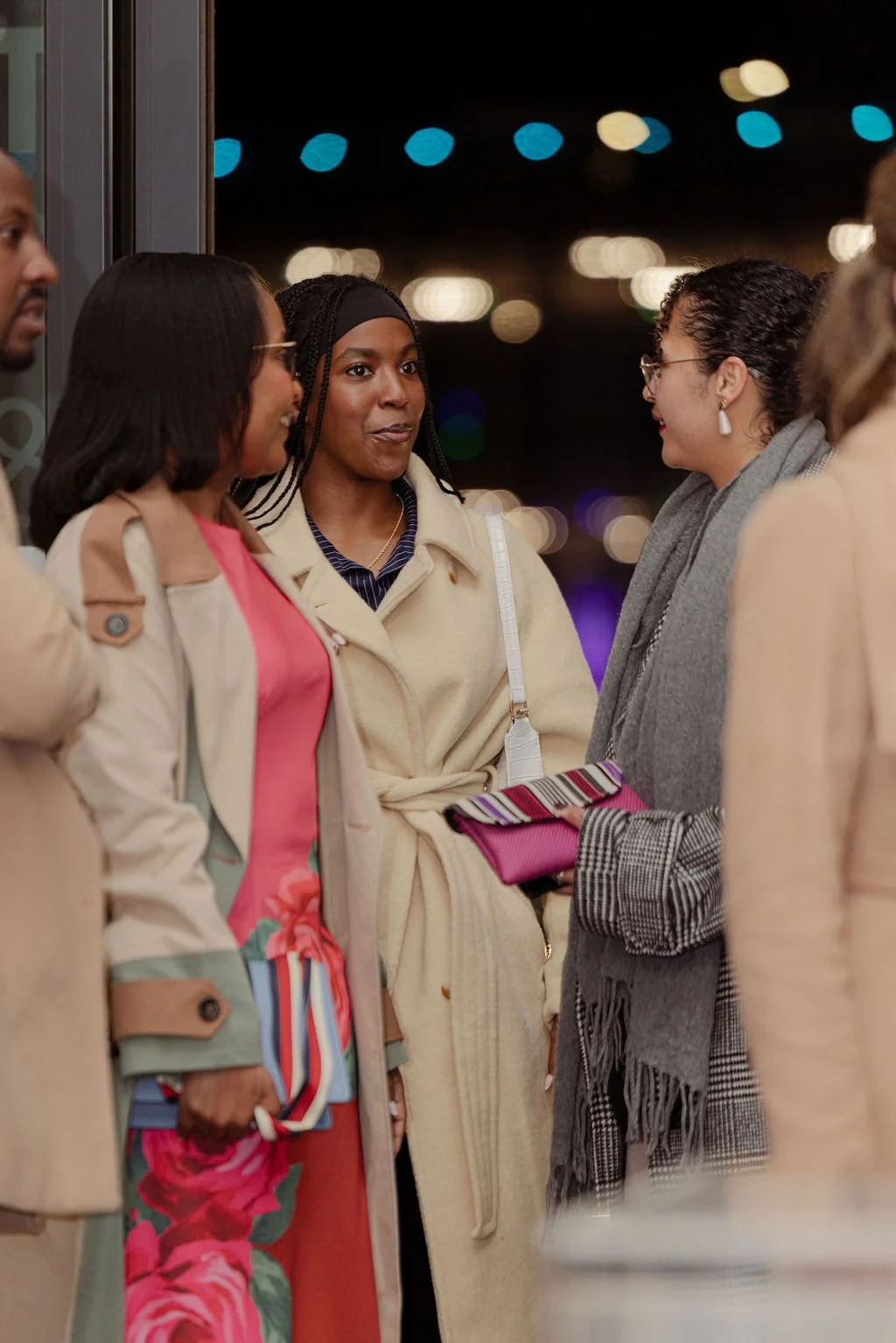 Group of women talking in an indoor setting at night, with blurred city lights in the background.