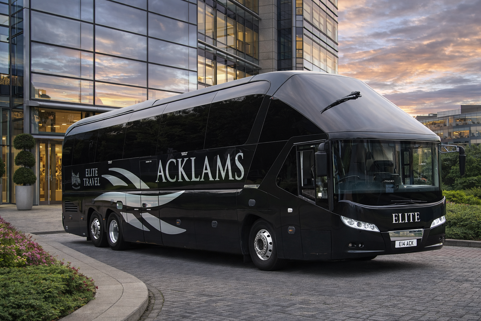 A black luxury tour bus with the words "ACKLAMS ELITE TRAVEL" written on its side, parked in front of a modern glass building during sunset.