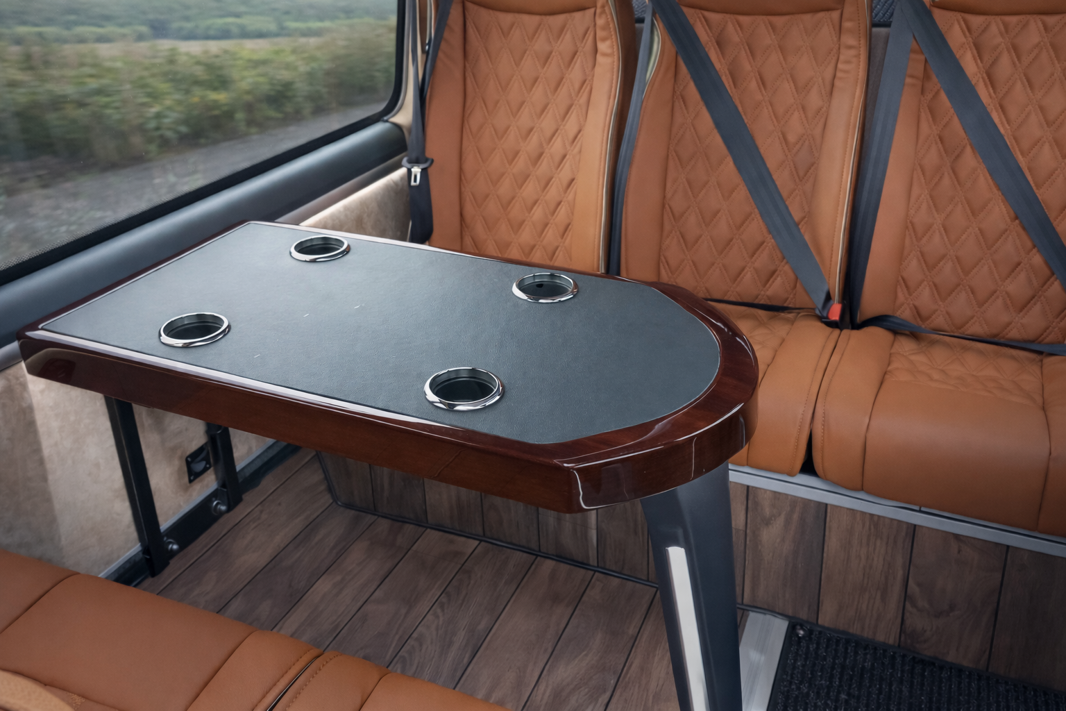 Interior of a vehicle with a table that has four cup holders, brown leather upholstered seats, and wood flooring.
