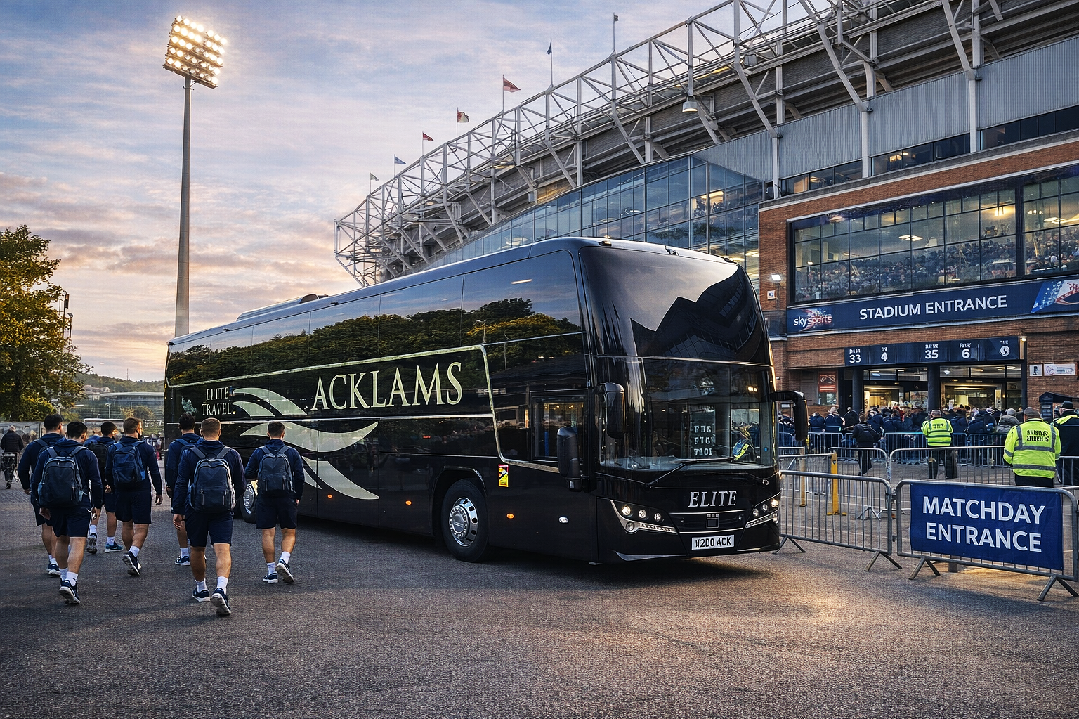 Soccer team players walking towards stadium entrance with team bus parked nearby, crowd and staff visible outside stadium.