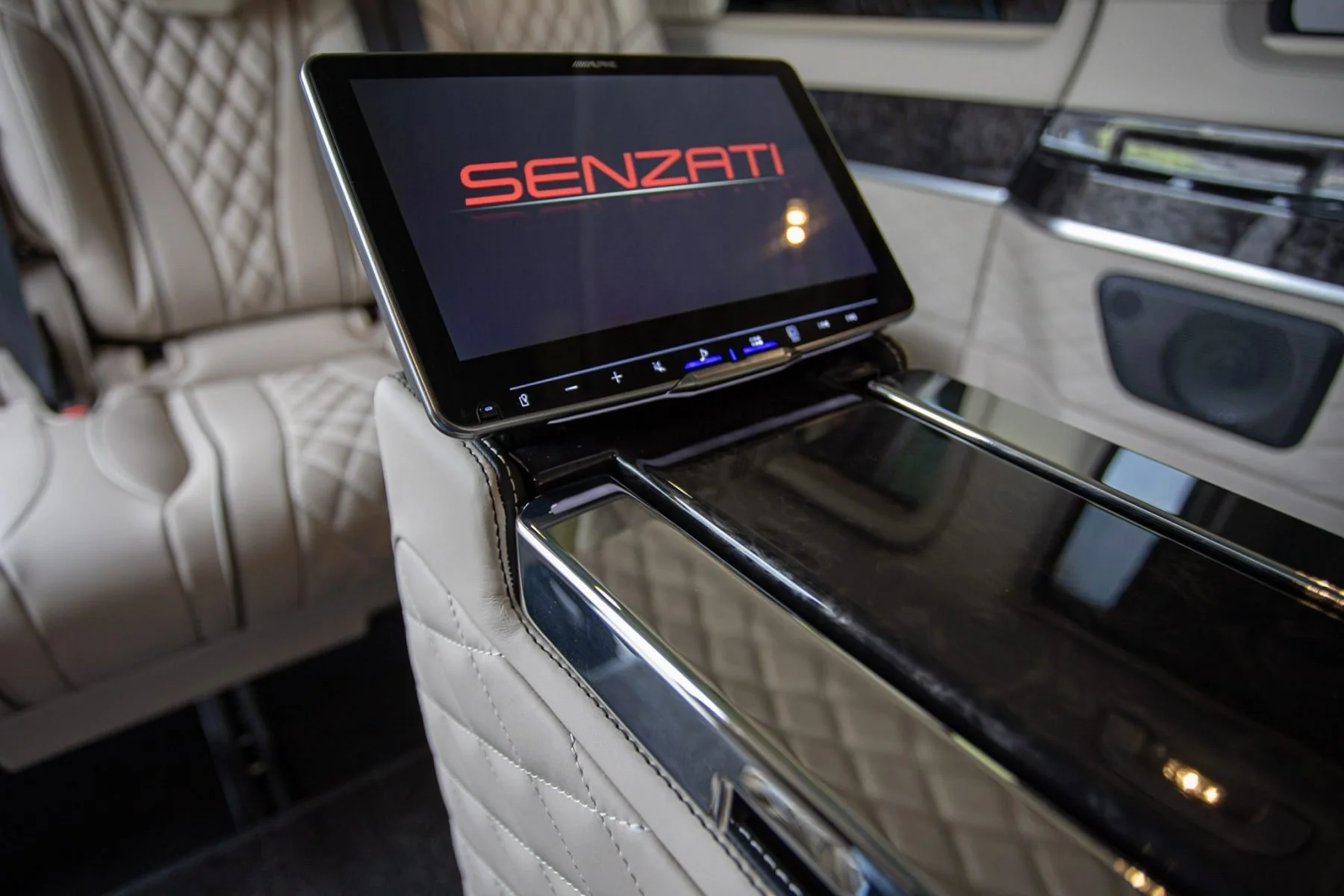 Interior of a luxury vehicle showing a mounted screen displaying the brand logo 'SENZATI' and a beige quilted leather seat.
