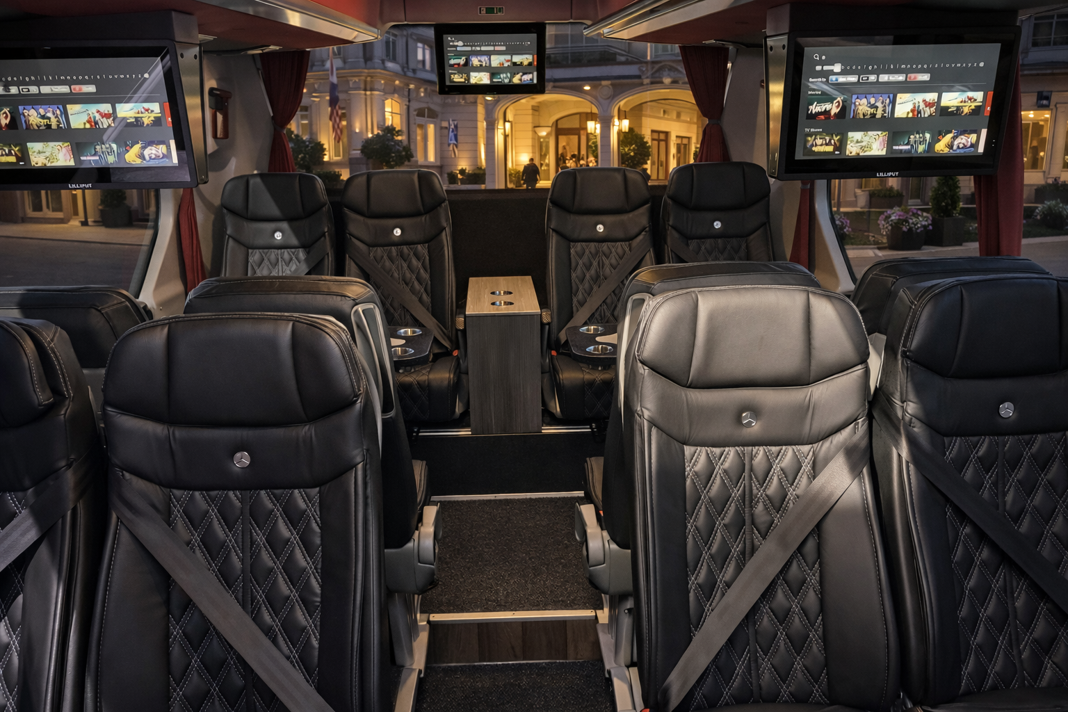 Interior of a luxury movie bus with black leather seats, two large screens displaying movies, and large windows showing a city street outside.