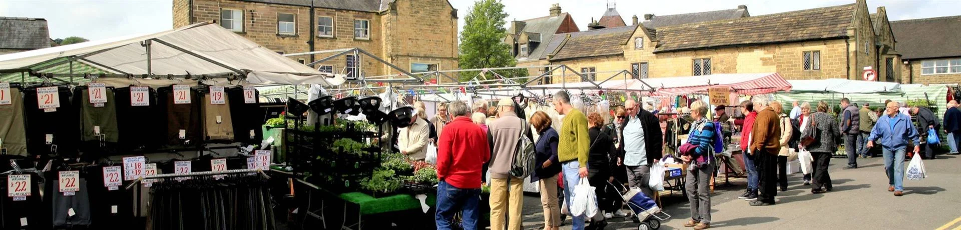 Outdoor market with stalls selling clothes and plants, and people shopping.