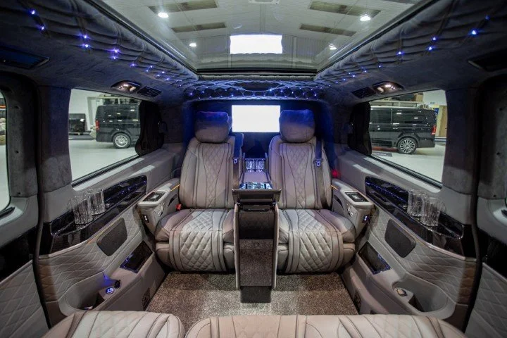 Luxury interior of a van with quilted seats, marble accents, and blue LED string lights on the ceiling.
