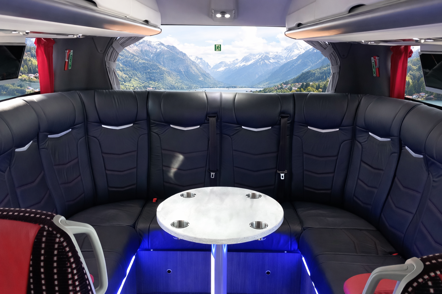 Inside a luxury vehicle with a curved black leather seating area, a small round white table, and scenic mountain view through the rear window.
