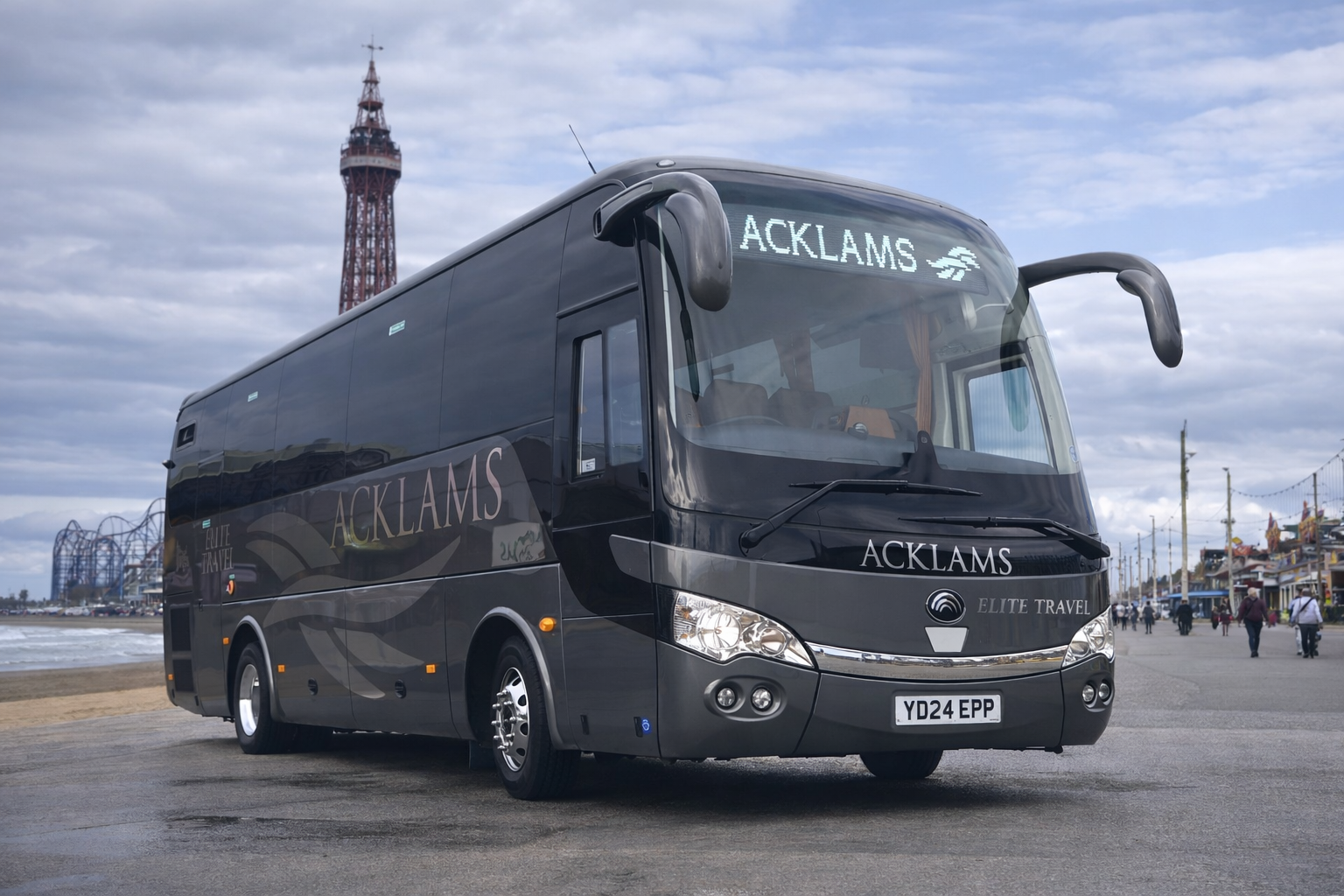 A black Acklams Elite Travel bus parked on a coastal boardwalk, with the beach and the SeaWorld San Diego roller coaster in the background.