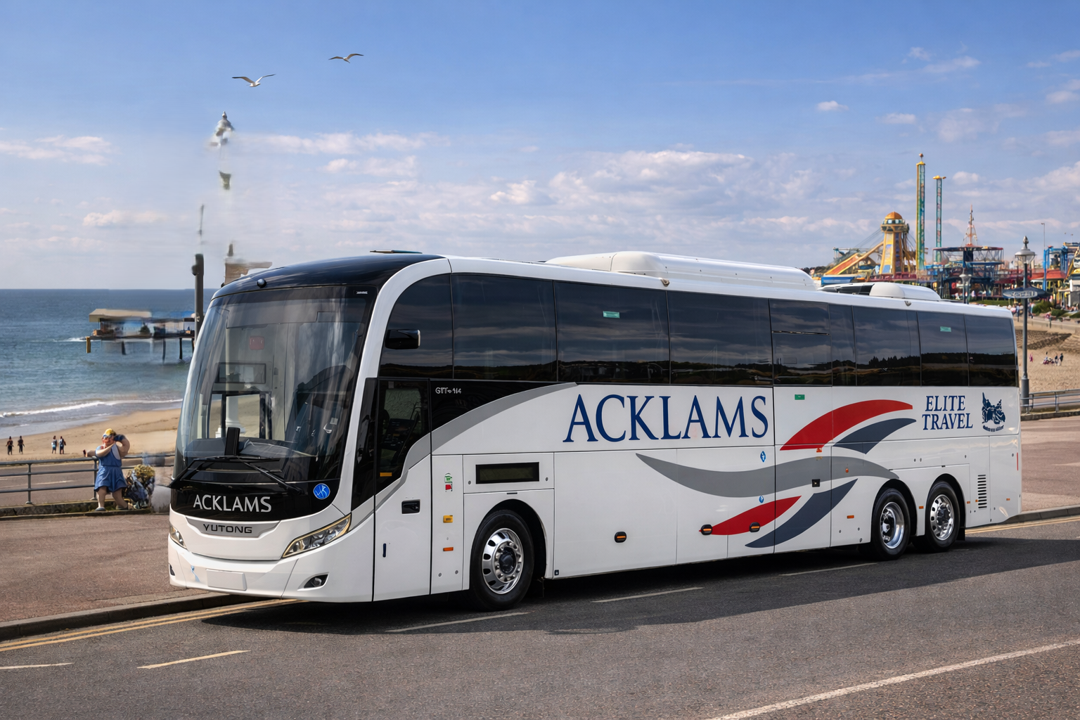 A white Acklams Elite Travel bus parked near a beach with a pier and amusement park rides in the background on a sunny day.