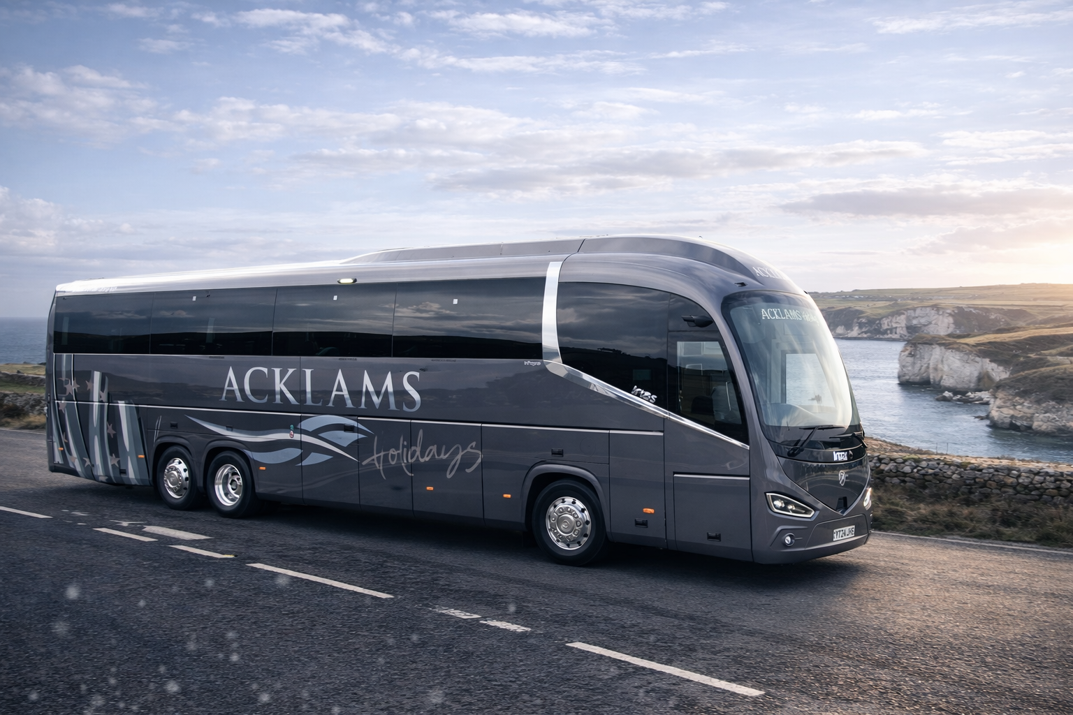 A modern gray sightseeing bus with the words 'ACKLAMS Holidays' on its side, traveling along a coastal road with cliffs and the ocean in the background during daytime.