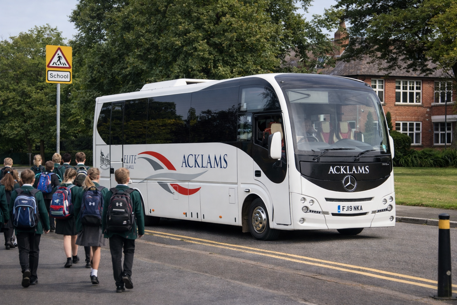 School children with backpacks boarding or disembarking from a white tour bus labeled 'Acklam's' in a suburban area with a 'School' pedestrian crossing sign and a brick house in the background.