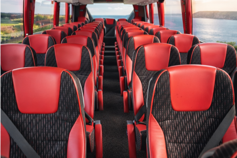 Inside a red bus with multiple rows of black and red seats, overlooking a river and green landscape through the windows.