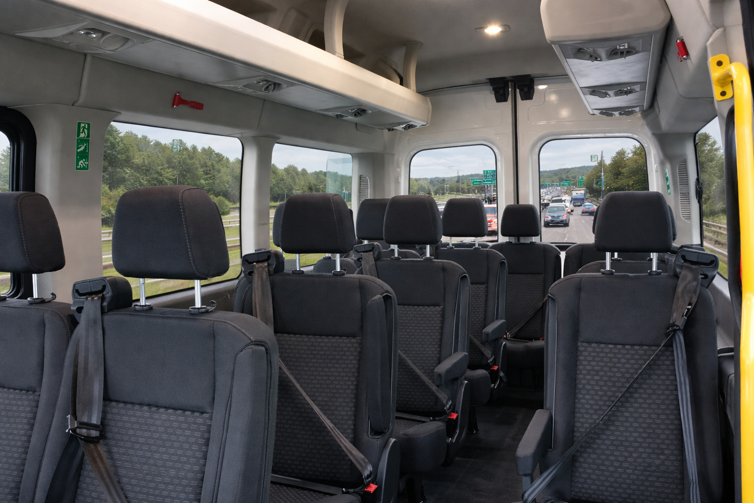 Interior view of a bus with multiple black seats and windows showing a highway with cars and green trees outside.