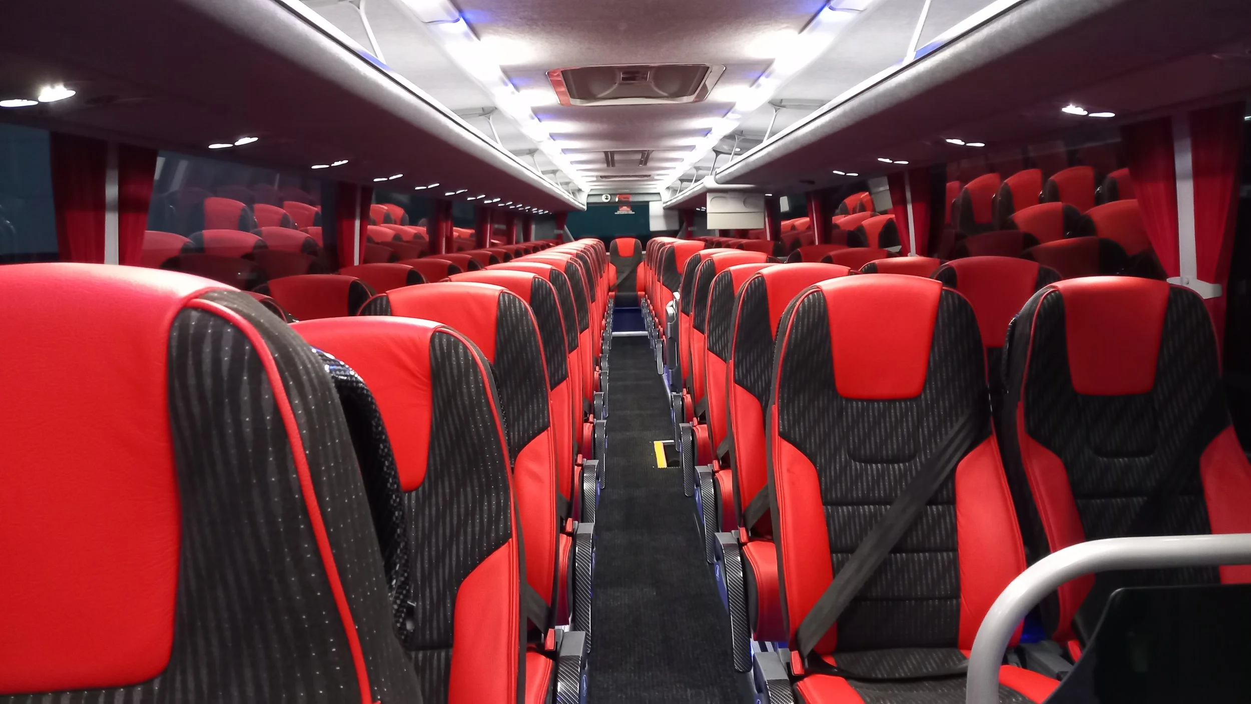 Interior of an empty bus with red and black seats, taken from the front looking towards the back.