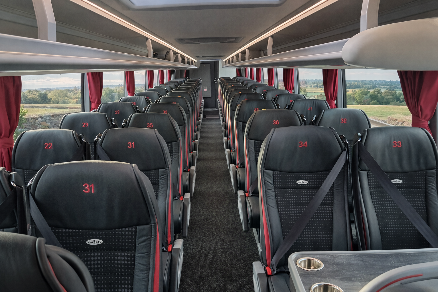 Empty bus interior with black seats, red numbers, and large windows showing a scenic view of fields and trees.