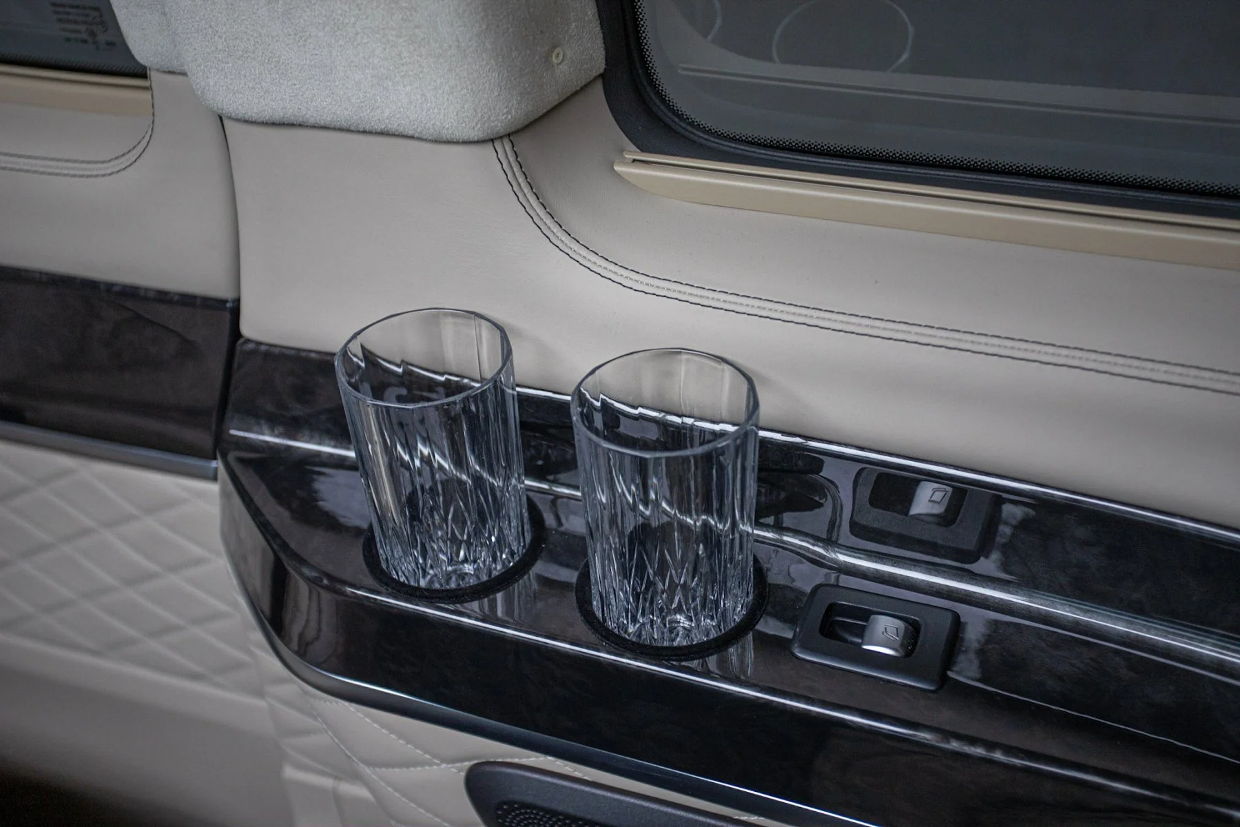 Two empty crystal glasses in cup holders on a black glossy surface inside a vehicle.