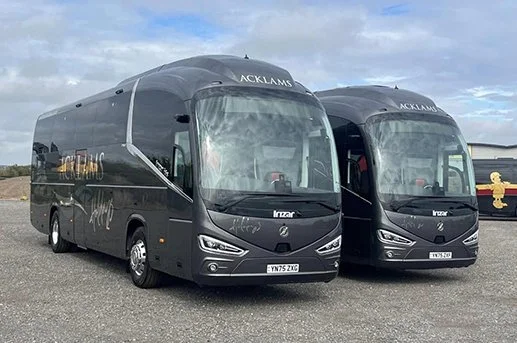 Two black tour buses parked on a gravel lot.