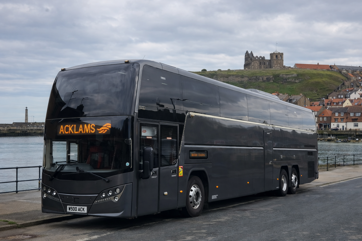 A black double-decker bus parked near the water with a cityscape and a hill with a castle in the background.
