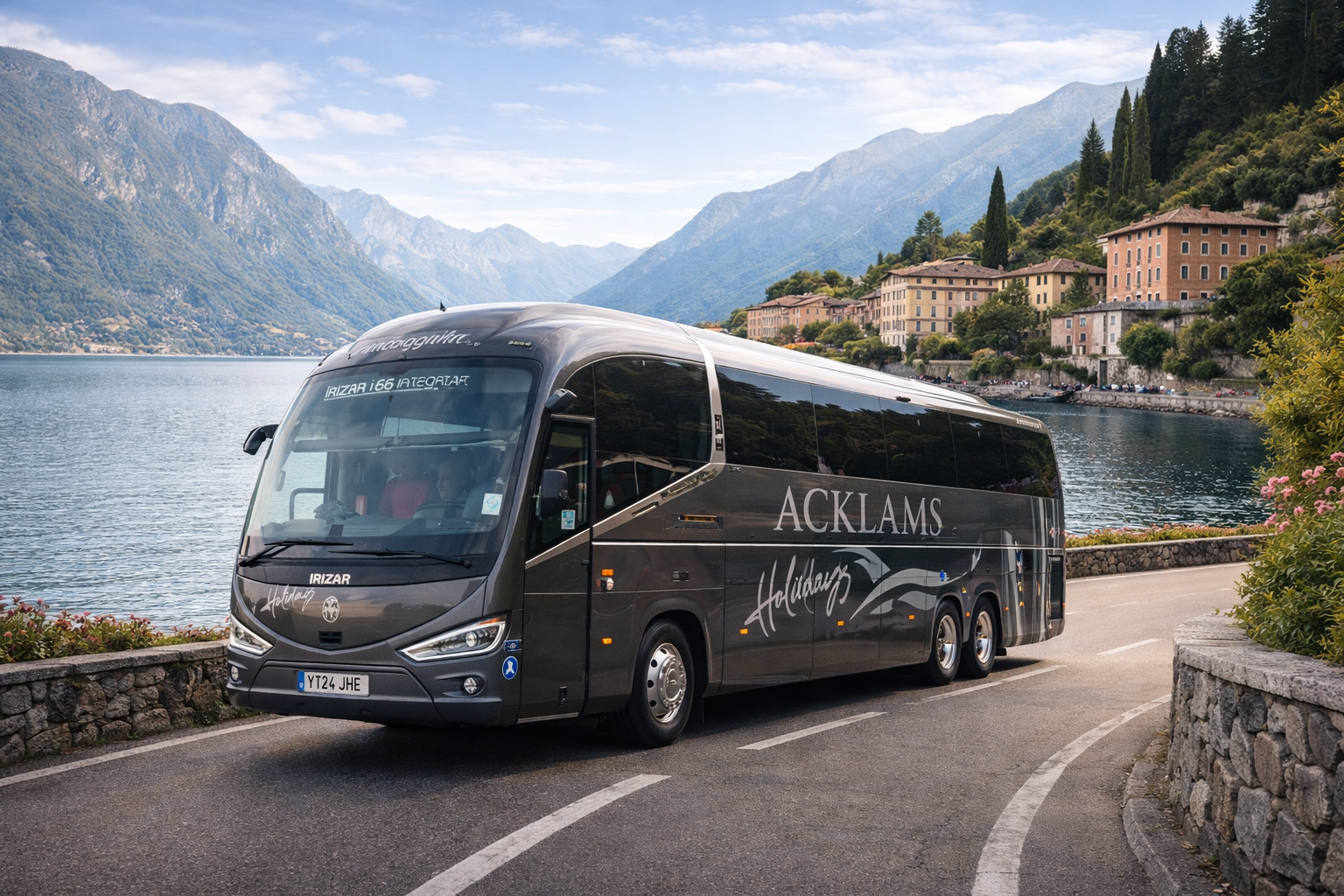 A black luxury bus labeled 'ACKLAMS Holidaying' driving on a scenic mountain road beside a lake, with colorful houses and lush green trees on the hillside in the background.