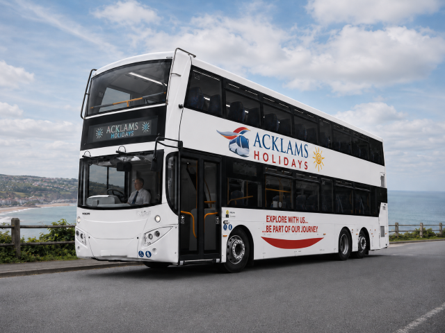 98 seat Double-decker bus branded with Acklams Holidays logo, traveling along a scenic coastal road with ocean and cliffs in the background, under a partly cloudy sky.