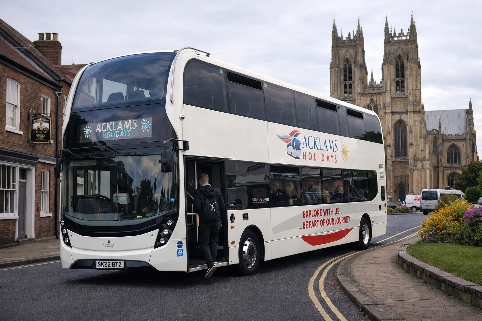 Double-decker white bus with 'ACKLAMS HOLIDAYS' logo and slogan 'Explore with us... Be part of our journey' parked on a street near a historic cathedral and houses, with a person boarding the bus.