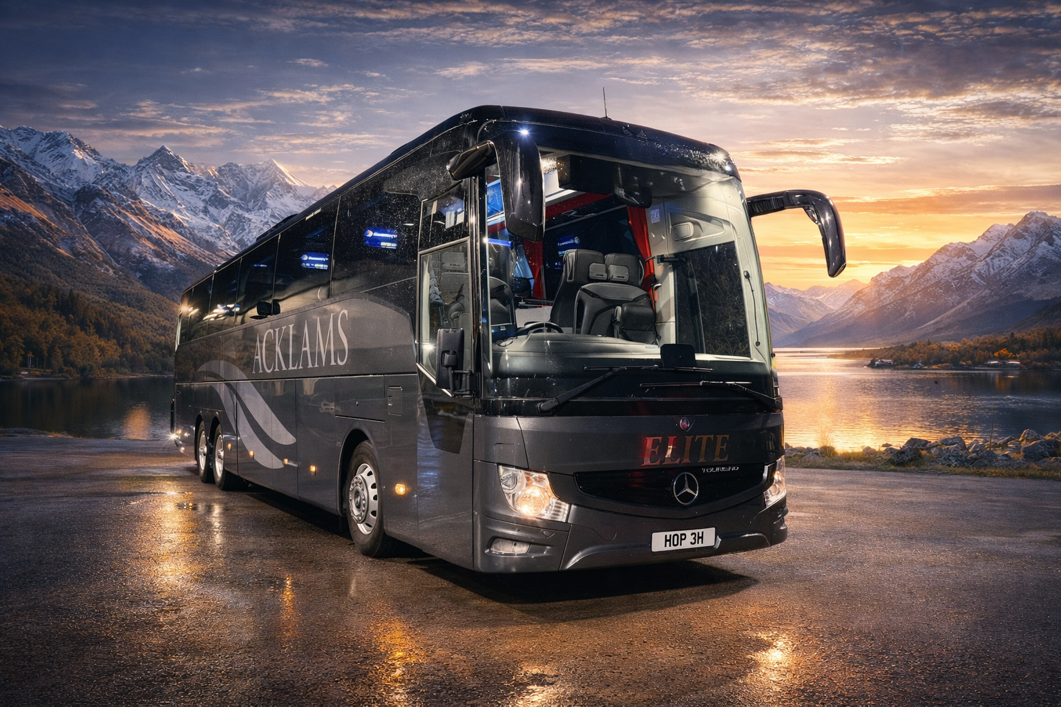 A black luxury bus parked by a lake with snow-capped mountains and a sunset sky in the background.