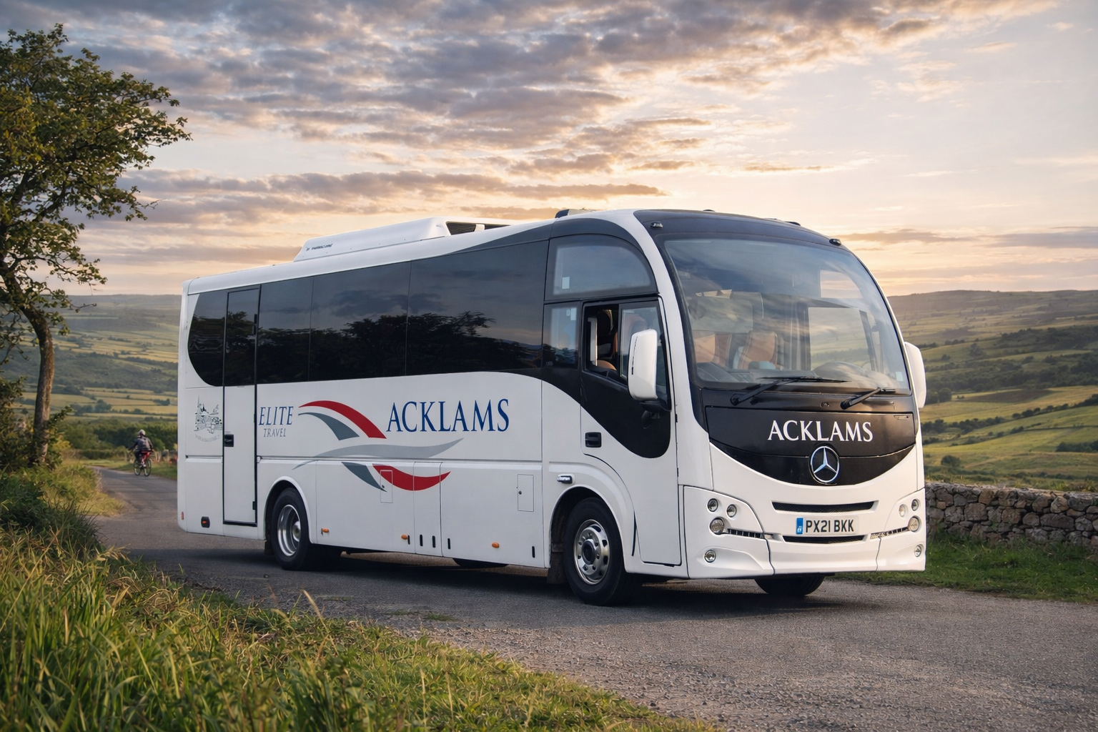 A white Mercedes-Benz coach bus with 'ACKLAMS' branding parked on a rural road during sunset.