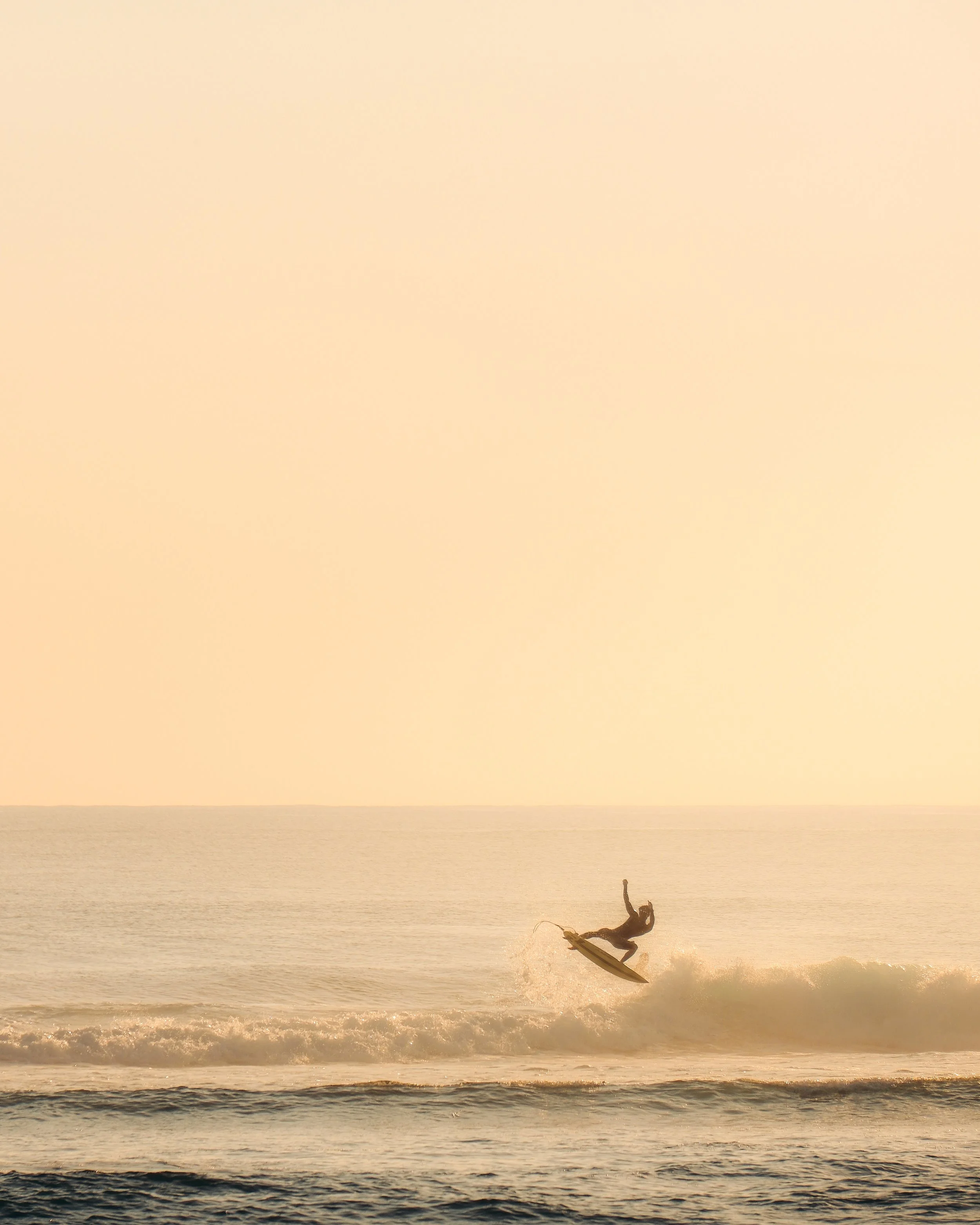 Surfer jumping on a surfboard in the ocean at sunset with a golden sky and waves.