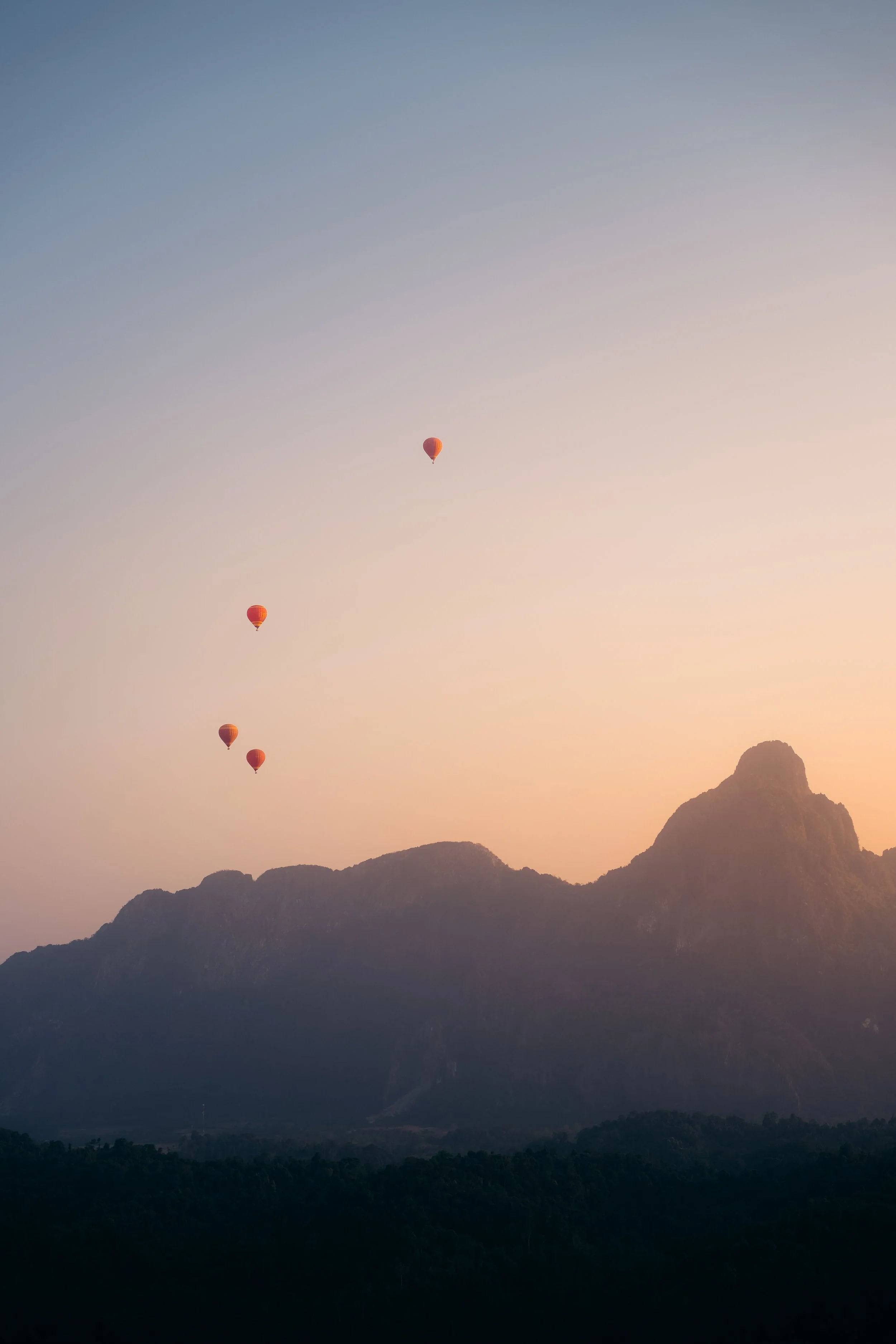 Four hot air balloons floating over a mountain at sunrise or sunset.