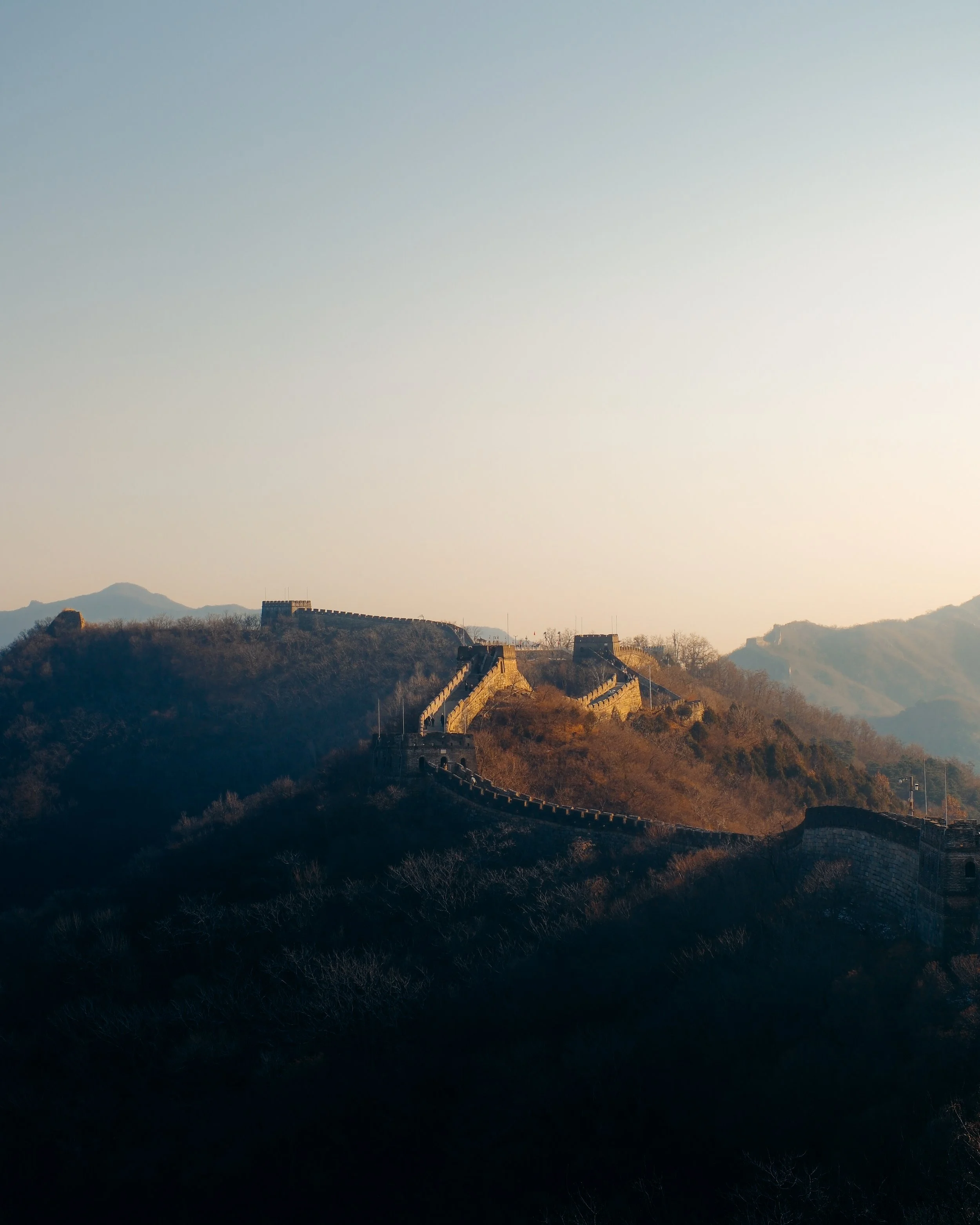 The Great Wall of China winding over mountain ridges during sunset.