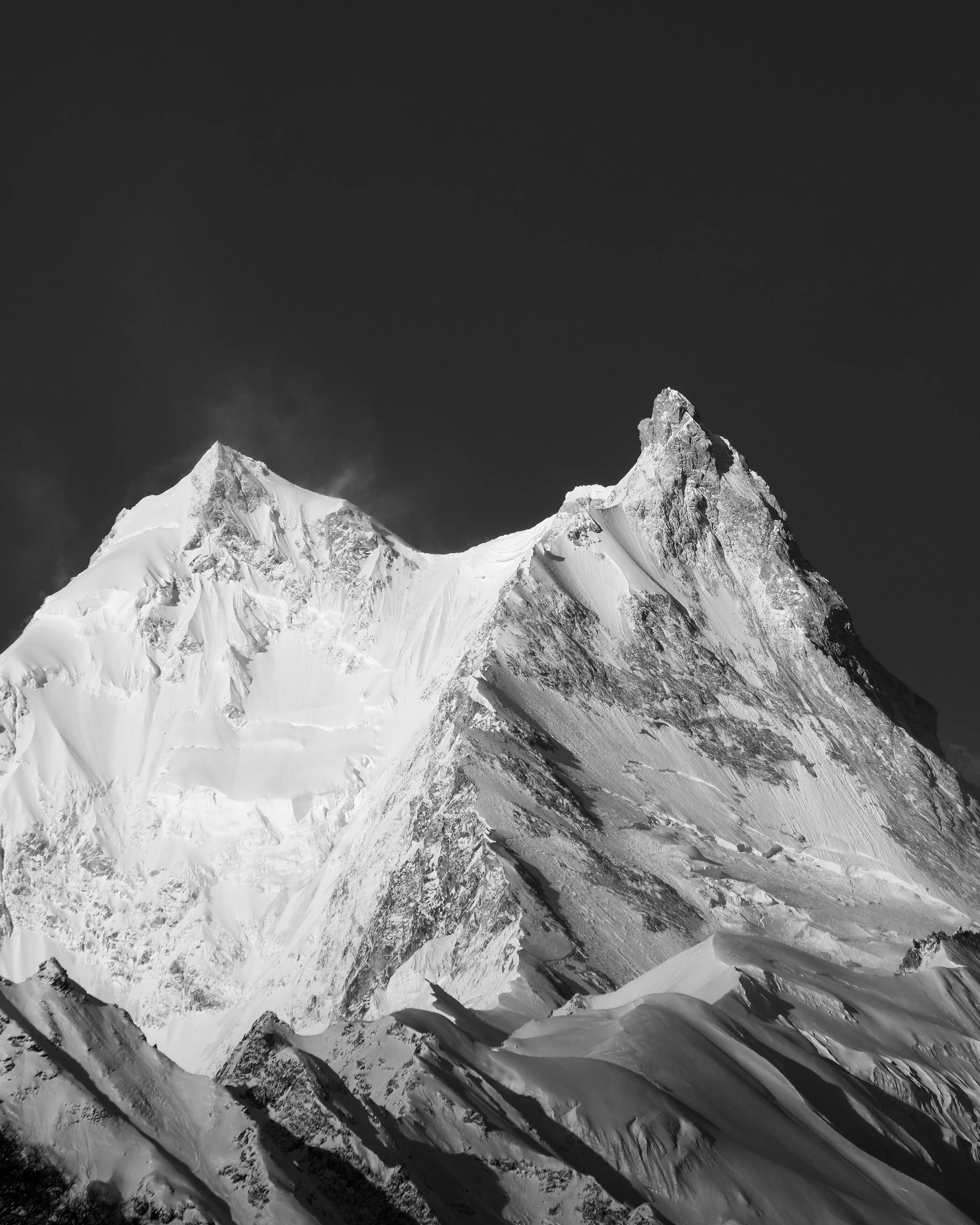 Black and white photo of snow-covered mountain peaks against a dark sky.