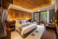 Luxury hotel room with a large bed, wooden accents, and a balcony with outdoor scenery.