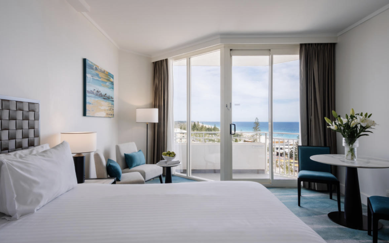 Hotel room with a large bed, a small sitting area, and a balcony view of the ocean.