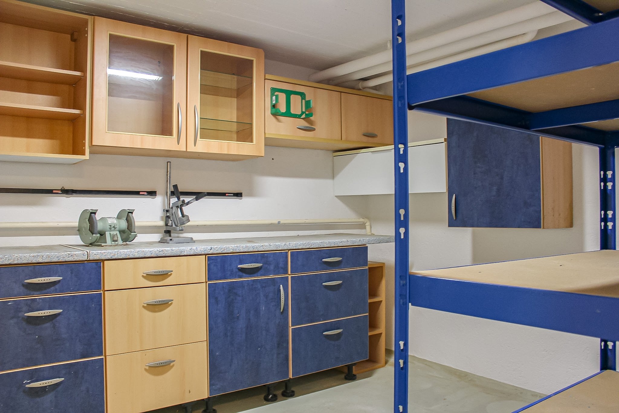 Ein Raum mit blauen und Holz-Küchenschränken, einem blauen Regal, einer Werkzeugmaschine und weißen Rohren an der Decke.