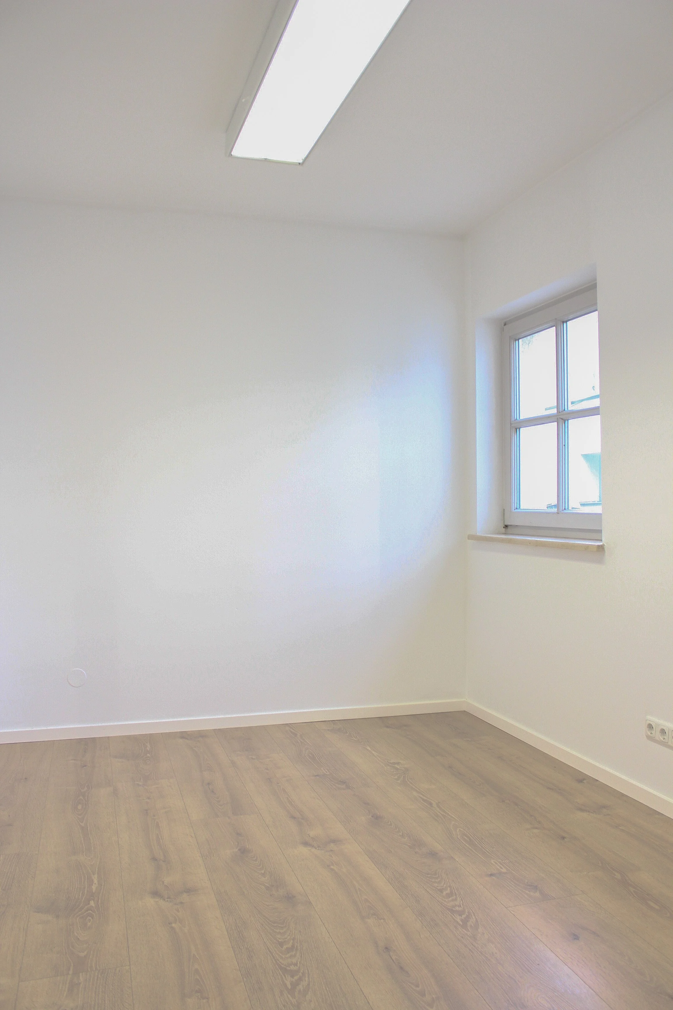 Ein leeres weißes Zimmer mit einer großen Fensterfront und einer Deckenleuchte.
