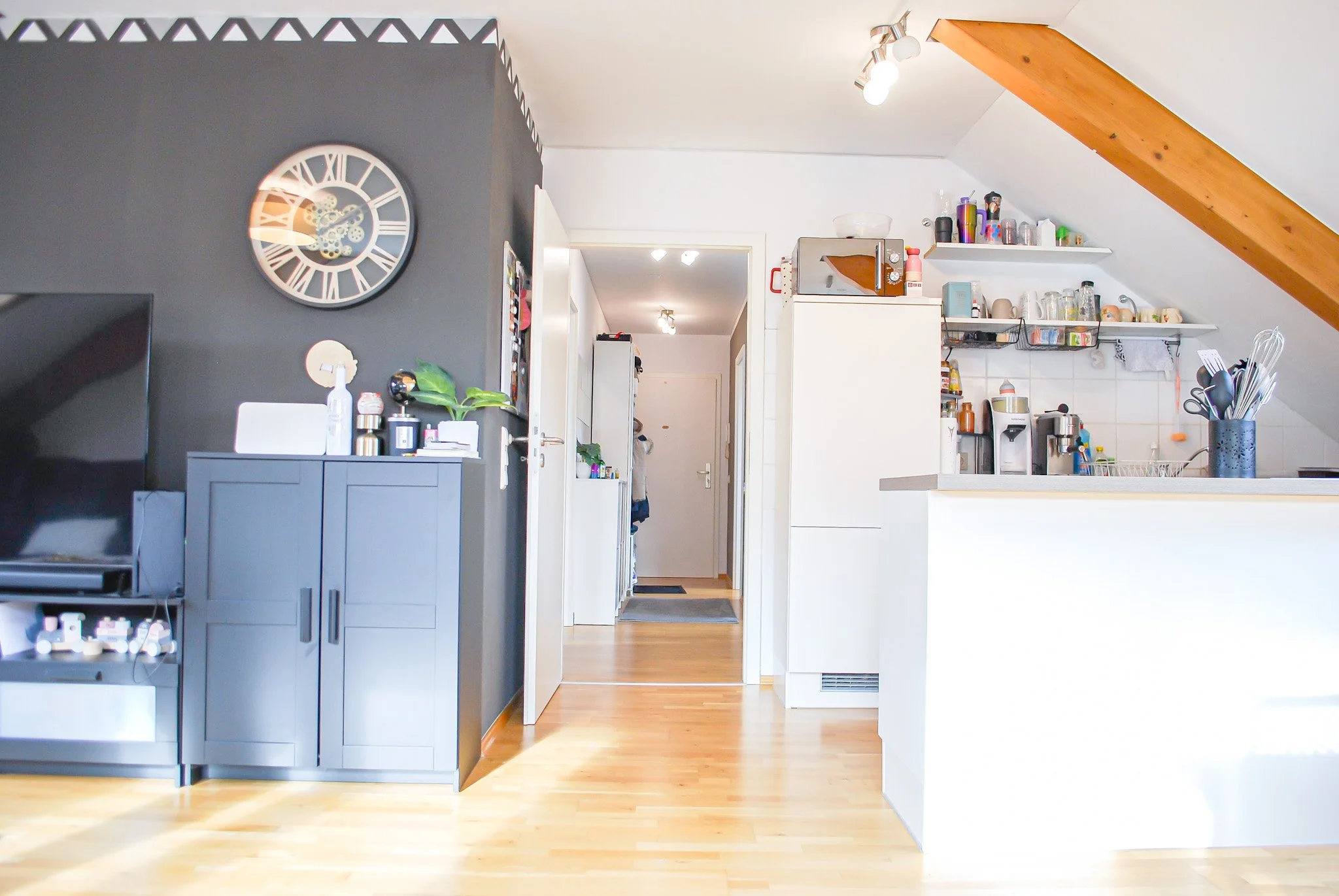 Küche mit weißen und grauen Möbeln, Holzdecke, gedeckter Boden, Wandregale mit Geschirr, Küchenutensilien und Kaffeeautomaten, moderner Stil, aufgeräumt.